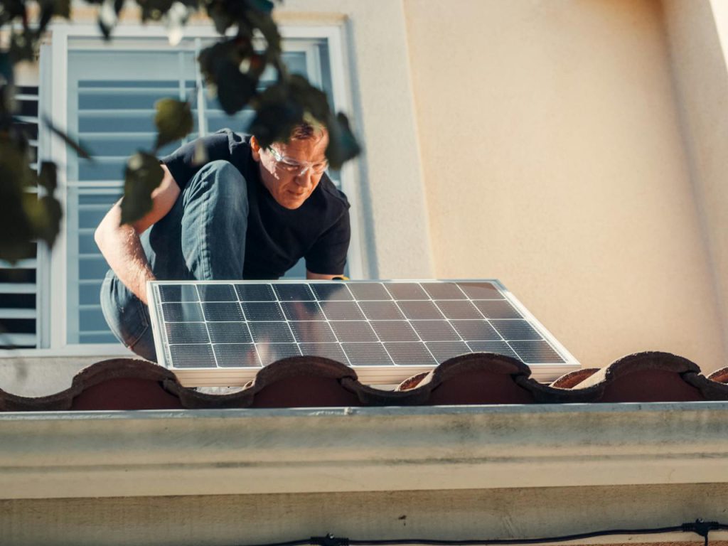 verduurzaam je woning: man op dak zonnepaneel installeren